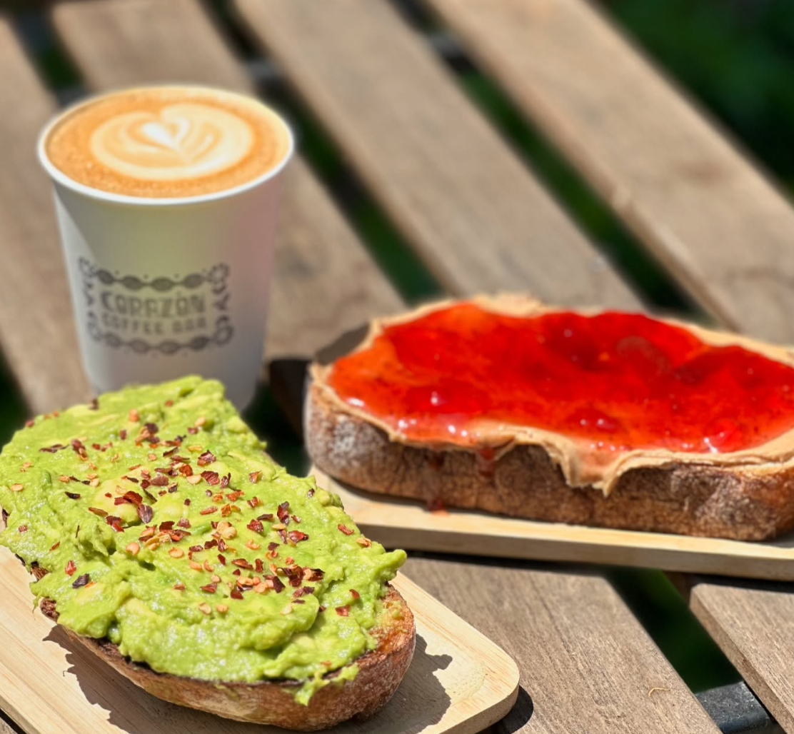 Avocado toast and strawberry toast on a wood picnic table outside Corazón